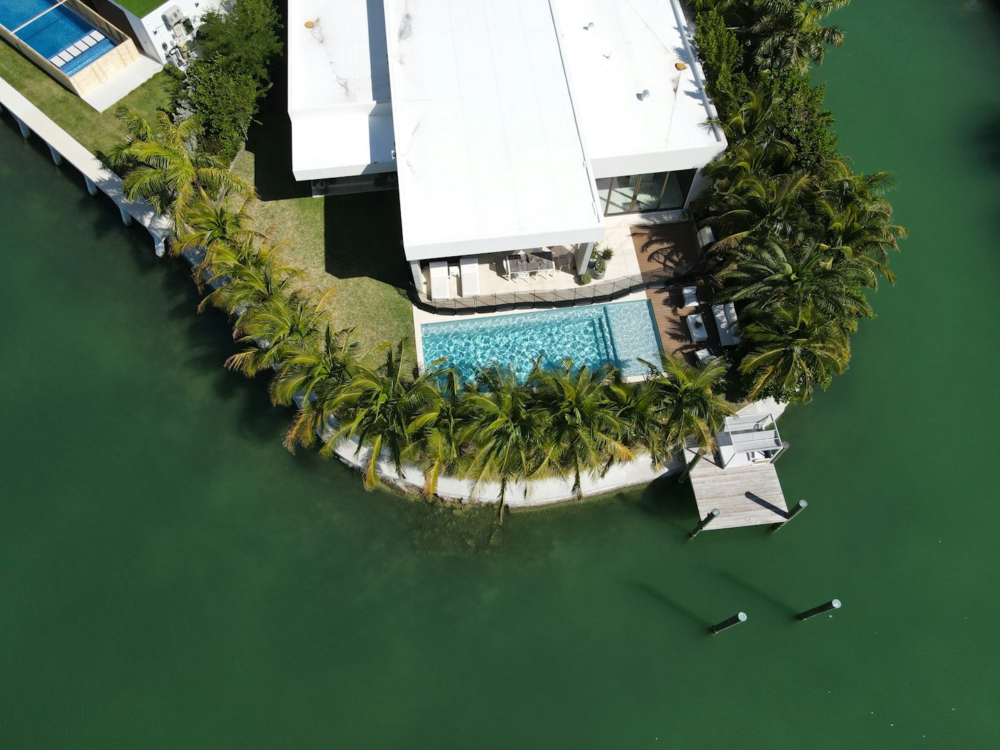 Modern white house with pools on a lush waterfront property.