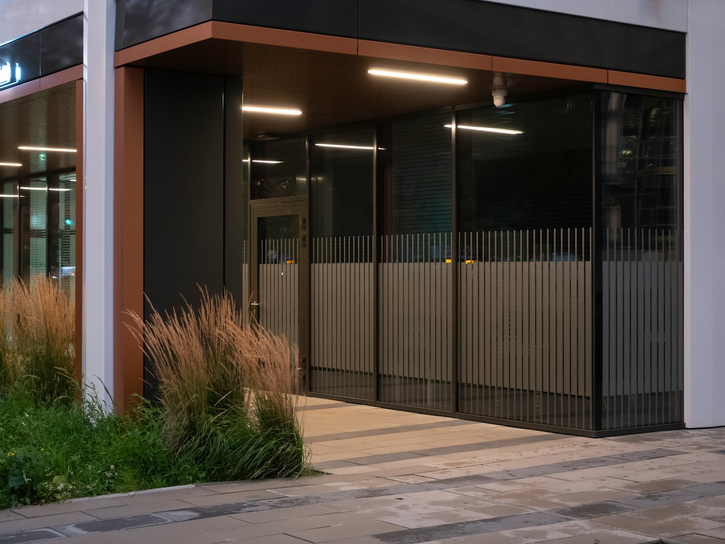 Modern building entrance with glass windows and lit landscaping.